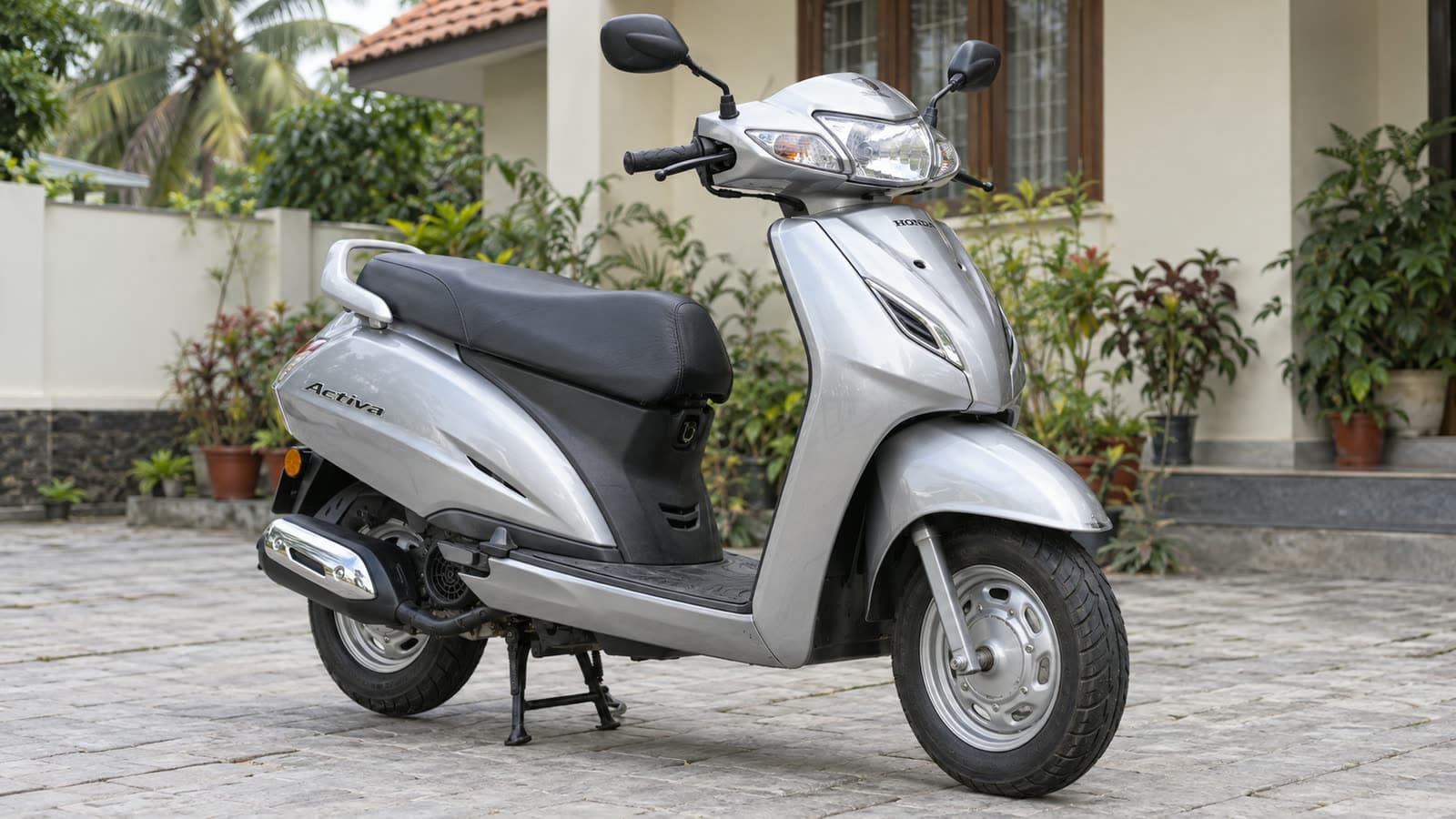 A silver Honda Activa scooter standing on a paved courtyard outside a Kerala house in daylight